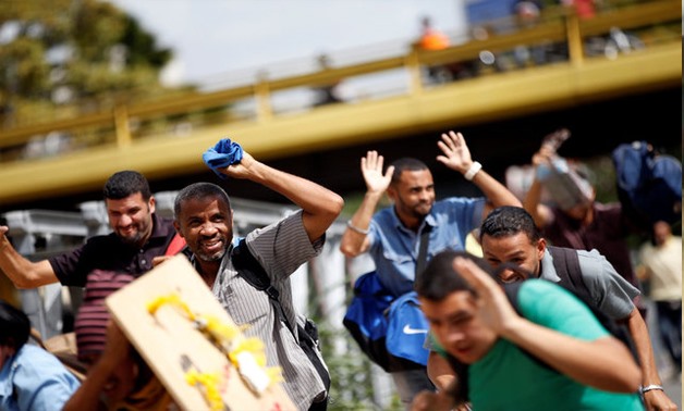 Demonstrators raise their hands as they run during a protest against Maduro's government in Caracas - Reuters
