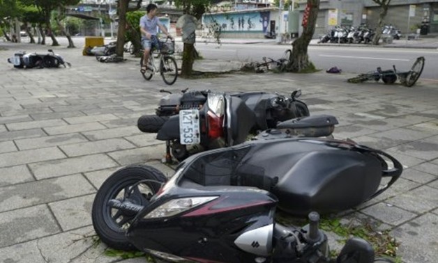 © AFP | A man rides past motorcycles and bikes on a pavement in New Taipei City after Typhoon Nesat slashed Taiwan
