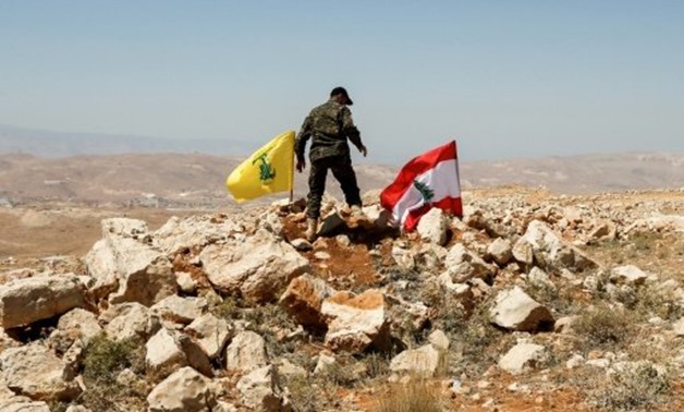 © AFP | A picture taken on an escorted tour by the Lebanese Shiite Hezbollah movement shows a fighter planting the group's flag and the Lebanese national flag in the Lebanese border area of Jurud Arsal on July 26, 2017
