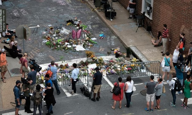 Mourners and passersby surround an impromptu memorial of flowers and chalk notes written on the street commemorating the victims at the scene of the car attack on a group of counter-protesters during the